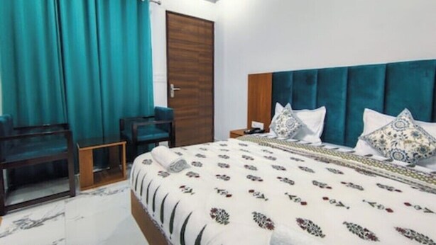 A bedroom with a bed, a nightstand, a desk, and a door. - Hotel Parth Inn (Rishikesh)