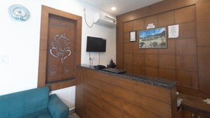 A reception area with a wooden reception desk, a flat-screen TV, a wall-mounted air conditioner, and a framed picture. - Hotel Parth Inn (Rishikesh)