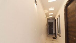 A hallway with a marble floor, recessed ceiling lights, and a wooden door on the right. - Hotel Parth Inn (Rishikesh)