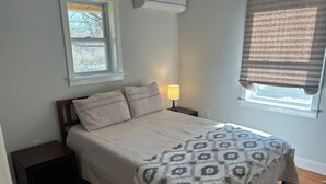 Un dormitorio con cama, mesitas de noche, lámpara, ventana y equipo de aire acondicionado.