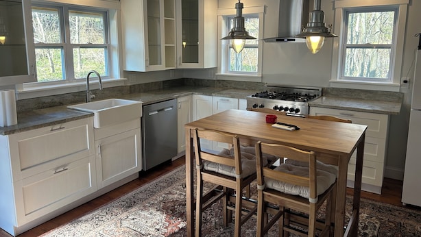 Una cocina moderna con armarios blancos, una estufa de acero inoxidable y una zona de comedor con una mesa y sillas de madera.
