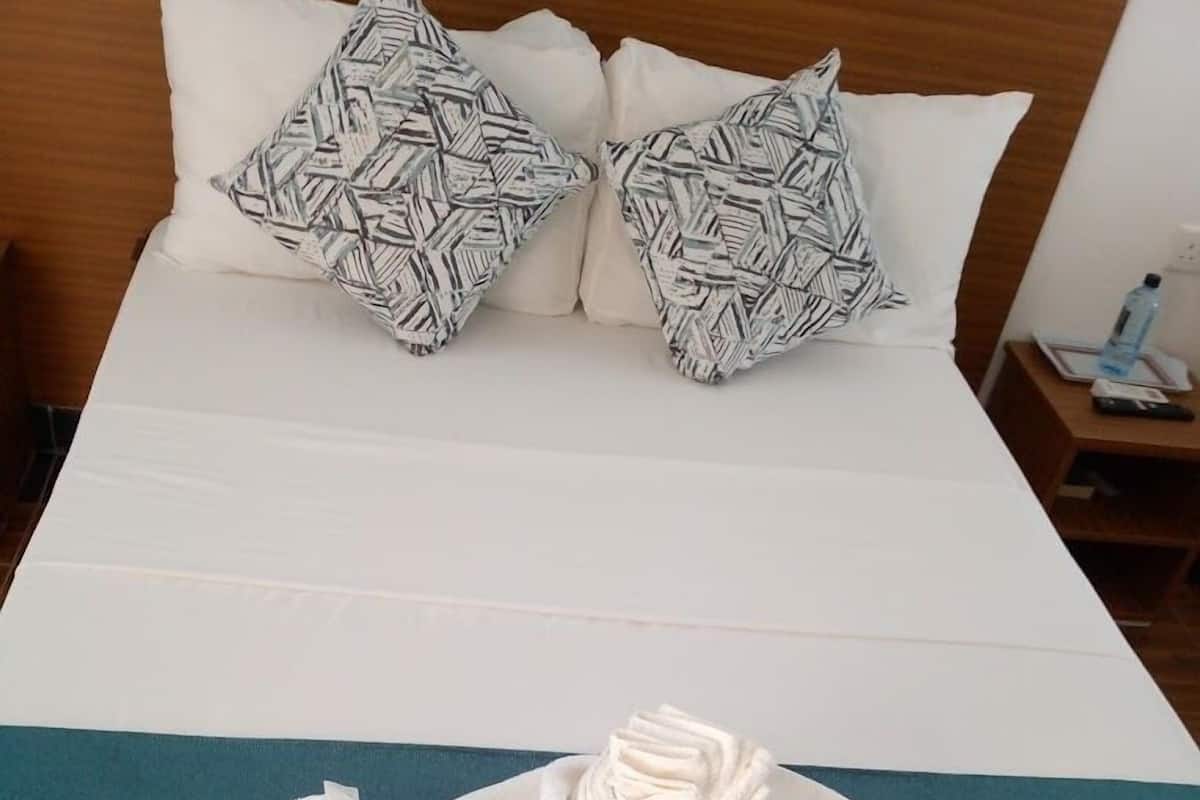A neatly made bed with a teal bedspread, two patterned pillows, and a rolled towel.