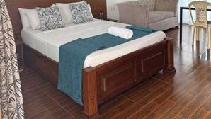 Habitación de hotel con una cama grande, un sofá, una silla, un ventilador de techo y una ventana con cortinas.