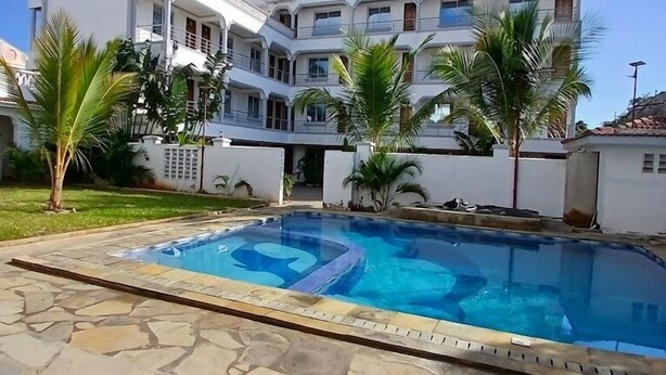 Un edificio de varios pisos con piscina, rodeado de palmeras y un patio de piedra.