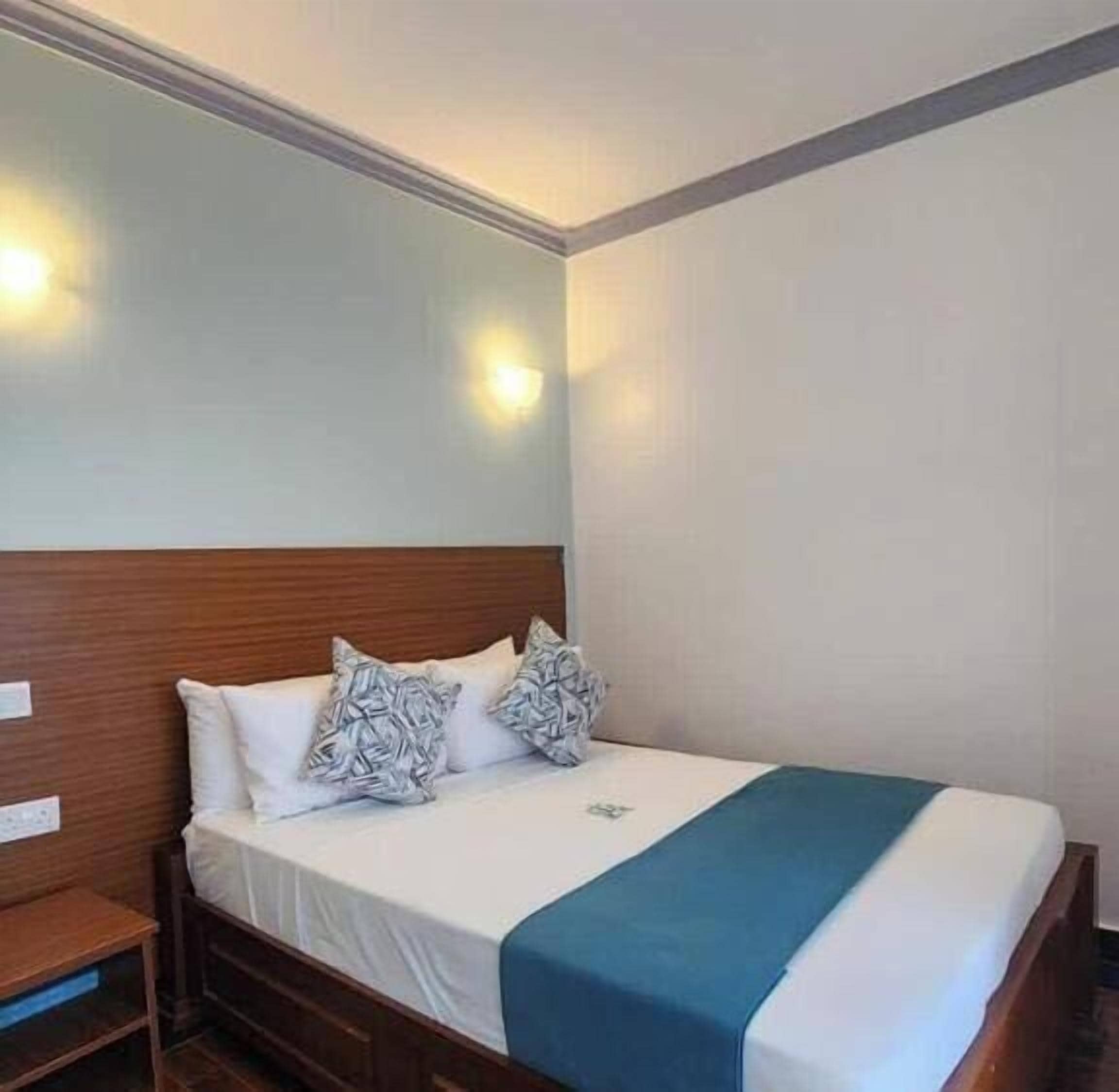 Habitación de hotel con cabecera de madera, colcha blanca y detalles azules.