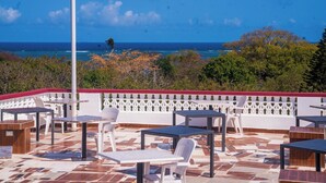 Un patio al aire libre con mesas y sillas, una cerca blanca y vista al océano.