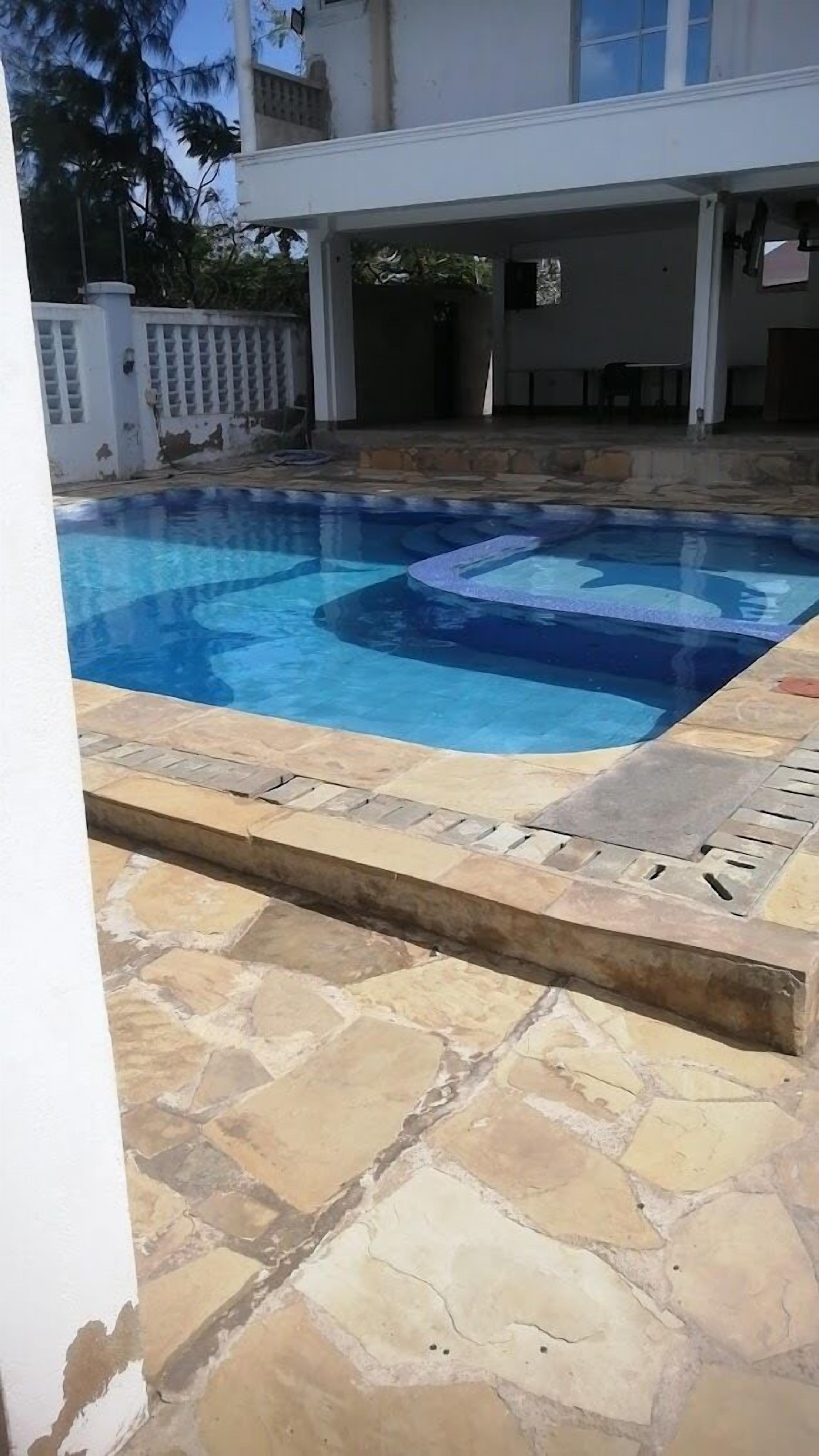 Une piscine aux carreaux de pierre, un bâtiment blanc en arrière-plan et une clôture blanche.