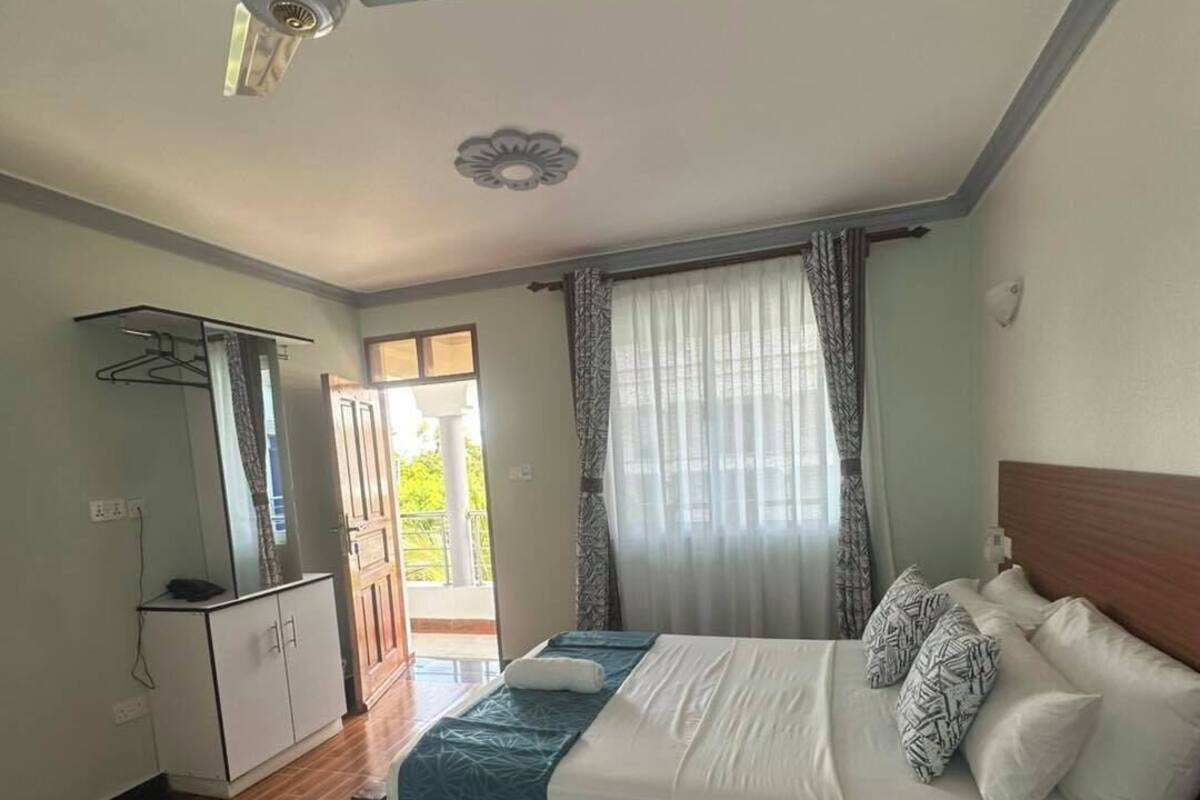 A bedroom with a bed, a ceiling fan, a wardrobe, and a window with curtains.