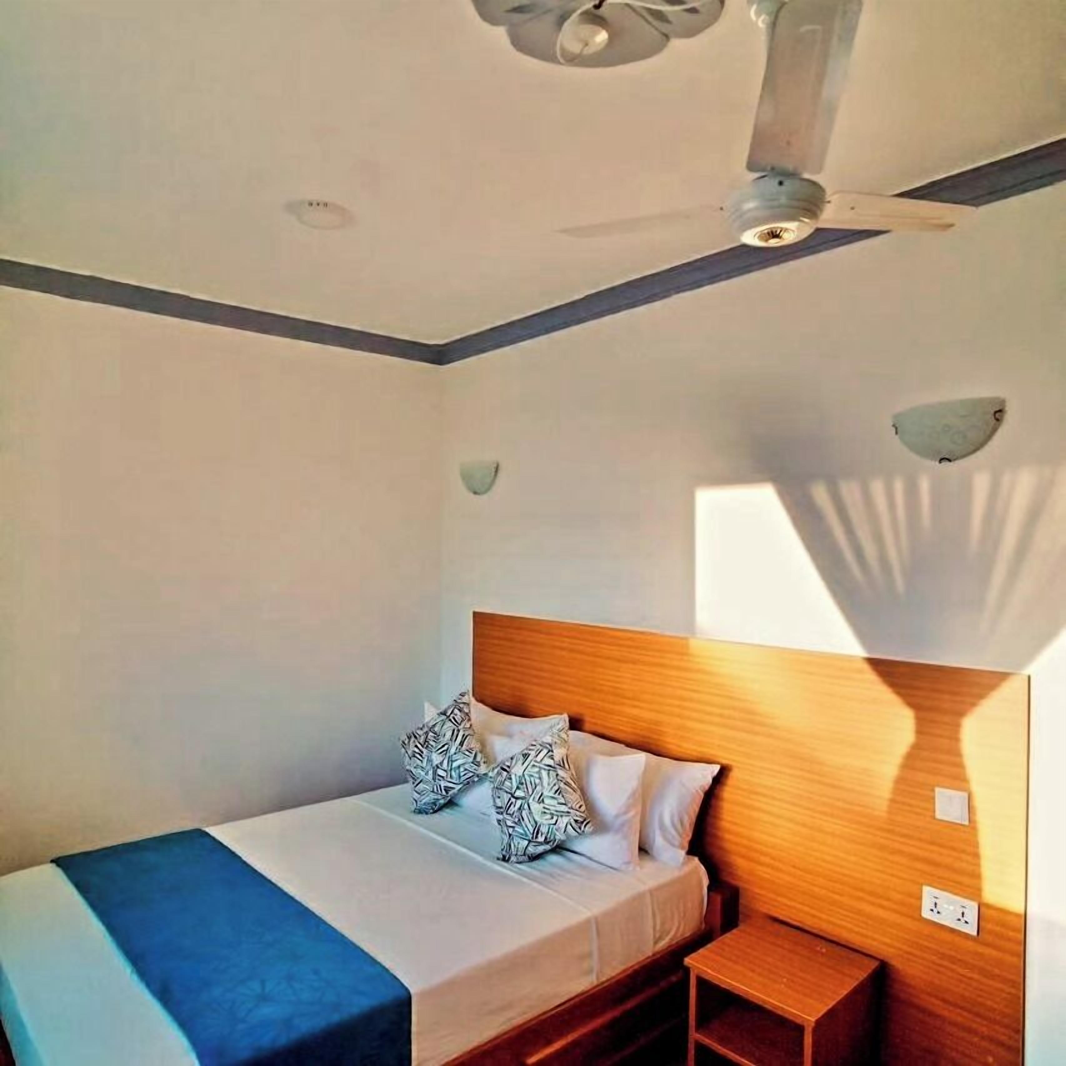 Een slaapkamer met een bed, nachtkastje en een plafondventilator.
