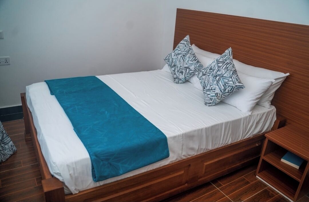 Un lit simple avec une tête de lit en bois, une literie blanche et des coussins à motifs.