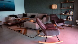 Ett modernt vardagsrum med en soffa, två gungstolar, ett soffbord och en bokhylla.