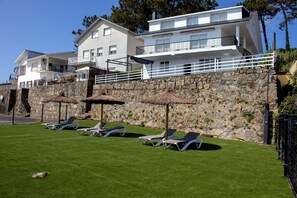 A modern building with a stone wall, a grassy lawn, and several lounge chairs.