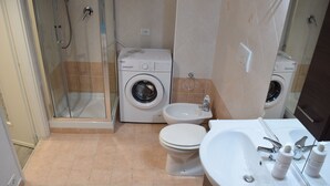 Un baño con cabina de ducha de vidrio, lavadora, bidé y lavamanos con espejo.