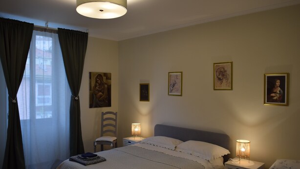 Un dormitorio con una cama, dos mesitas de noche, una silla y una ventana con cortinas.