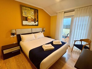 A hotel room with a bed, a nightstand, a lamp, a chair, and a view of the outdoors. - Hotel Reigosa (Ponte Caldelas)