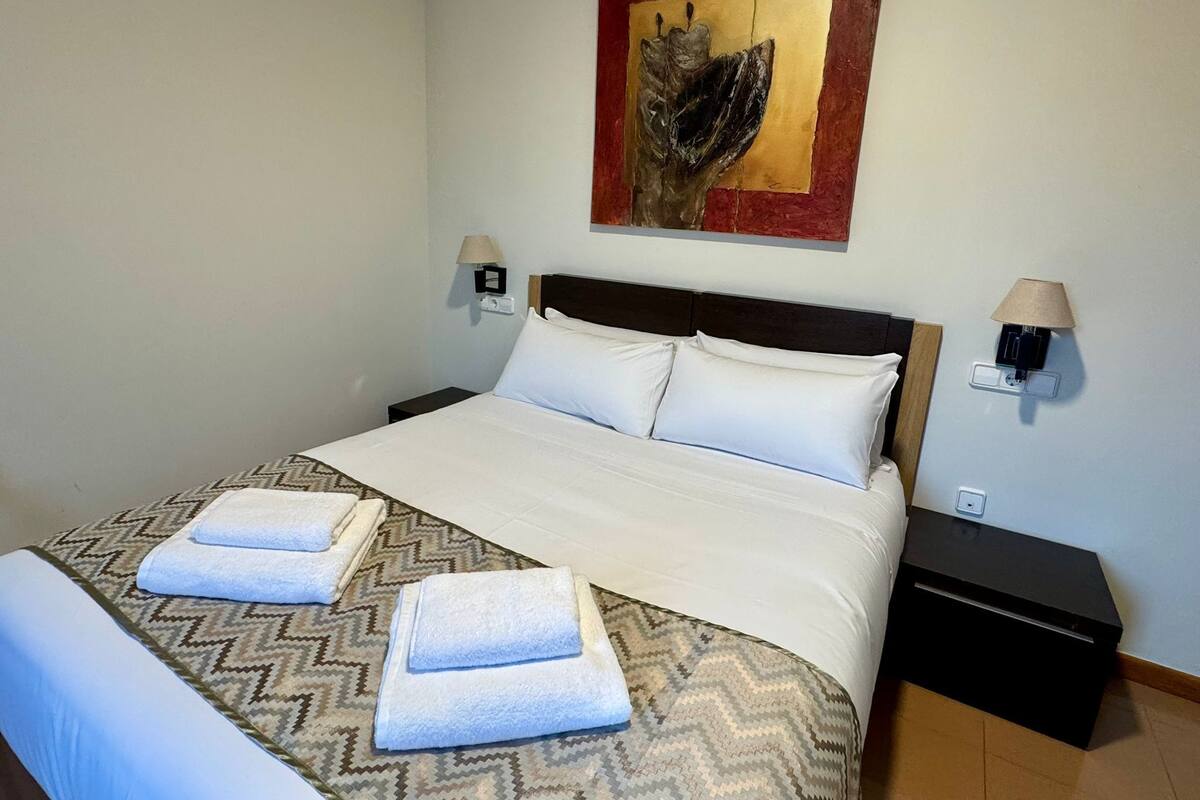A hotel room with a bed, two bedside lamps, a wall-mounted artwork, and a nightstand.