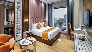 Hotelkamer met een bed, een bureau, een stoel, een televisie en uitzicht op de stad.