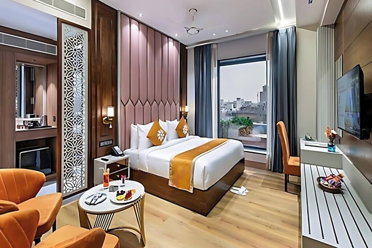 Habitación de hotel con cama, escritorio, silla, televisor y vistas a la ciudad.