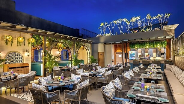 Een terras met zitgedeelte en tafels van riet, een bar met een aanrecht, en een decoratief plafond met plantenmotieven.