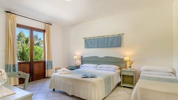 A bedroom with a bed, bedside tables, a chair, a window with curtains, and a view of greenery outside.