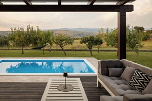 Ein Poolbereich mit einer Liege und einer Lampe, umgeben von einer Holzterrasse und Blick auf eine hügelige Landschaft.
