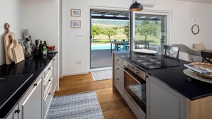 Une cuisine moderne dotée d’un grand îlot central, d’un coin repas offrant une vue agréable et d’une porte-fenêtre coulissante donnant sur une terrasse extérieure.