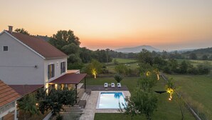 Une maison avec une piscine, un espace salon extérieur et une vue sur la campagne au coucher du soleil.