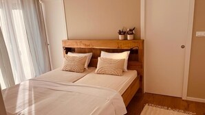Une chambre avec deux lits, une tête de lit en bois, une table de chevet avec des plantes et une porte.
