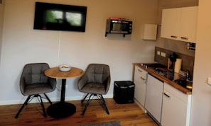 Cocina compacta con microondas, un lavamanos pequeño y una zona de comedor con dos sillas y una mesa.