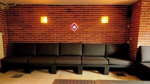 Eine Ziegelwand mit zwei Wandleuchten und einem schwarzen Sofa mit Kissen.
