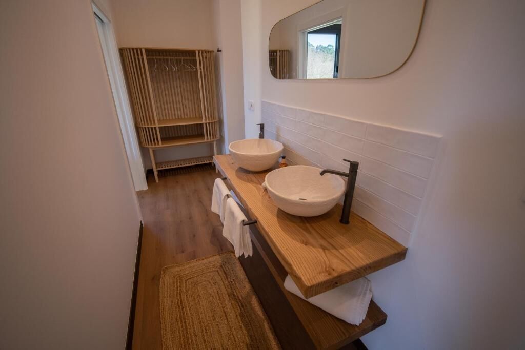 Un baño moderno con dos lavamanos, un mueble de tocador de madera, un perchero para toallas y un espejo grande.