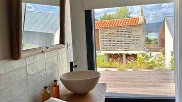 A bathroom with a large mirror, a wooden vanity, a bowl sink, and a view of a house through a glass door.