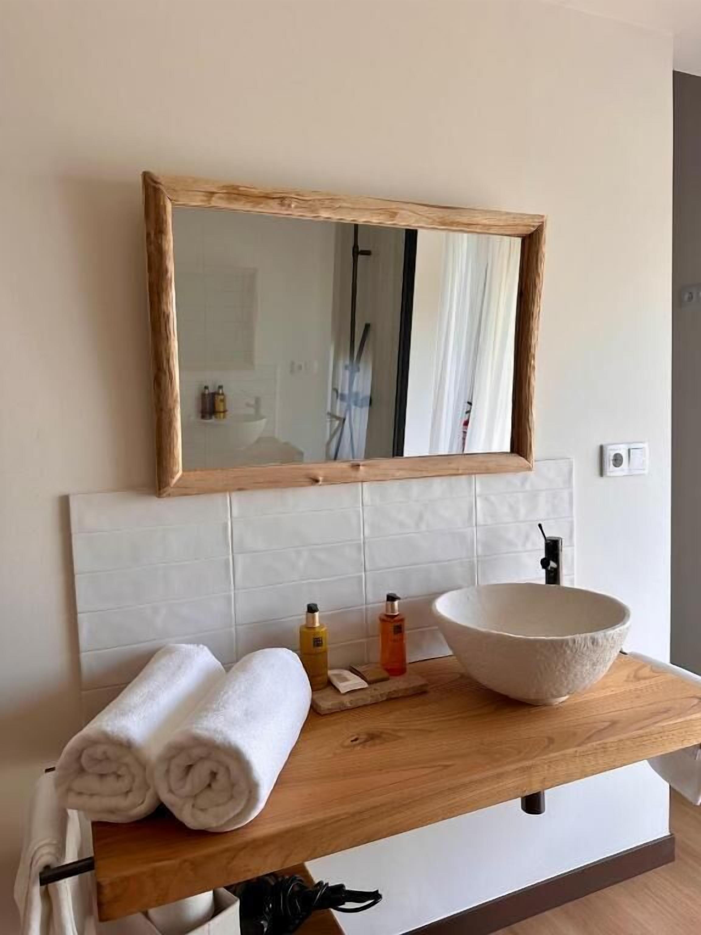 Un meuble-lavabo pour la salle de bain avec un plan de toilette en bois, un grand miroir et un lavabo sur colonne.