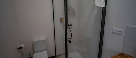 A modern bathroom with a glass-enclosed shower, a toilet, and a wooden vanity.