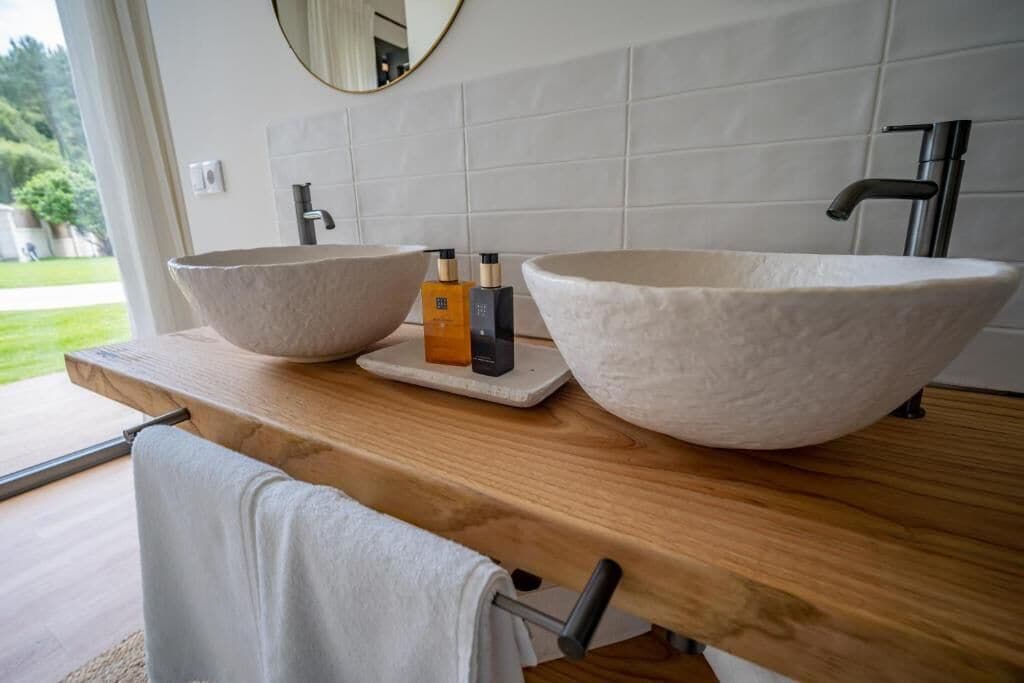 A bathroom with two large stone sinks, a wooden countertop, a towel rack, and a mirror.