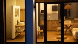 Une cuisine moderne avec des meubles en bois, un coin repas comprenant une table et des chaises, et une salle de bain séparée dotée d’un grand miroir et d’un lavabo.