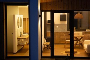 Una cocina moderna con armarios de madera, un comedor con mesa y sillas, y un baño independiente con un espejo grande y lavamanos.