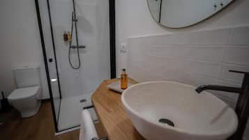Een moderne badkamer met een douchecabine van glas, een witte wastafel en een spiegel aan de muur.