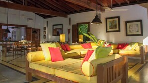 A spacious living area with a high ceiling, wooden beams, a sofa set, a dining area, and a view of the outdoors. - Saffron House: Private Seafront Villa with Infinity Pool & Tropical Gardens (Dikwella)