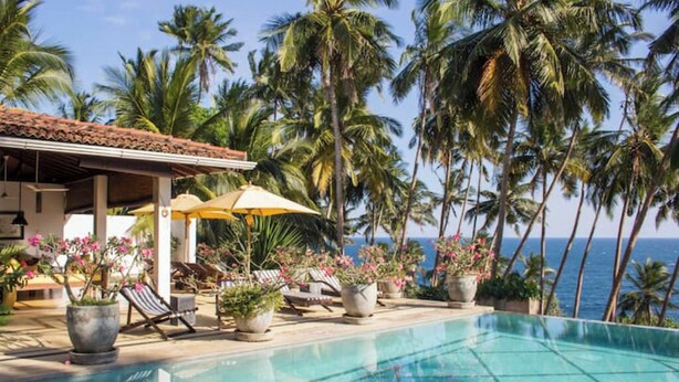 A pool area with lounge chairs, umbrellas, and potted plants. - Saffron House: Private Seafront Villa with Infinity Pool & Tropical Gardens (Dikwella)