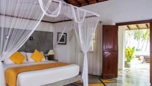 A room with a bed, white canopy, yellow pillows, a grey headboard, and a wooden door. - Saffron House: Private Seafront Villa with Infinity Pool & Tropical Gardens (Dikwella)