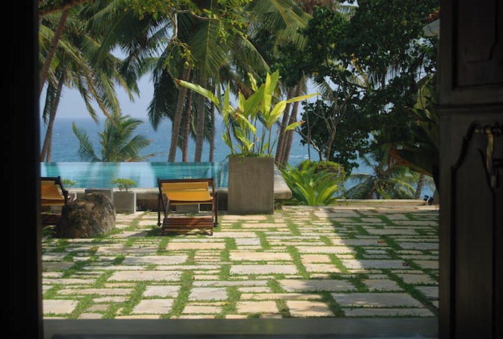 A tropical outdoor area with a pool, lounge chairs, and palm trees.