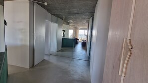 Un pasillo con un muro espejado, un banco verde y vista a una habitación con un ventanal grande.