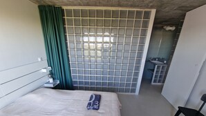 Habitación de hotel con cama, una silla, baño con lavamanos y vistas al exterior.