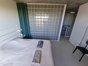 A hotel room with a bed, a chair, a bathroom with a sink, and a view of the outside. - Exceptional rooftop overlooking the sea (La Grande-Motte)