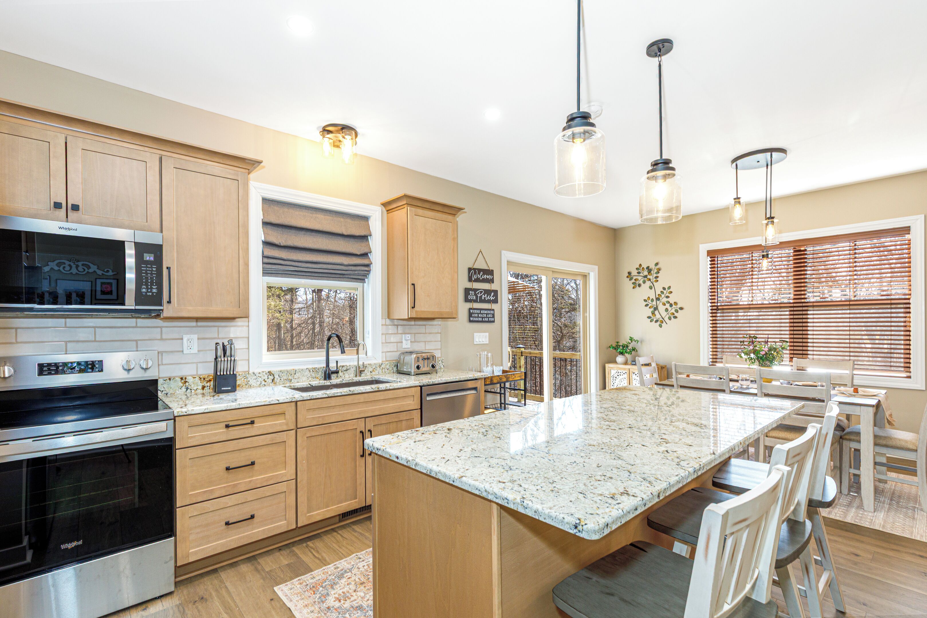 A modern kitchen with wooden cabinets, stainless steel appliances, a large island, and pendant lighting.