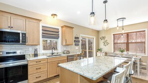 Una cocina moderna con armarios de madera, electrodomésticos de acero inoxidable, una isla grande e iluminación colgante.
