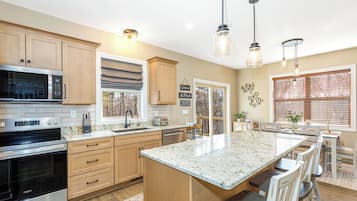 A modern kitchen with wooden cabinets, stainless steel appliances, a large island, and pendant lighting.