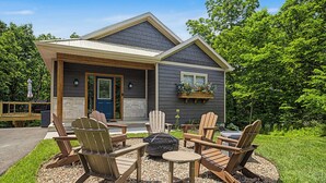 Una casa con un porche cubierto, mobiliario exterior con sillas Adirondack y un brasero.