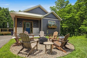 A house with a covered porch, outdoor seating with Adirondack chairs, and a fire pit. - Modern New Construction ~ Private Hot Tub, Fire Pit, Gas Grill (Galena)